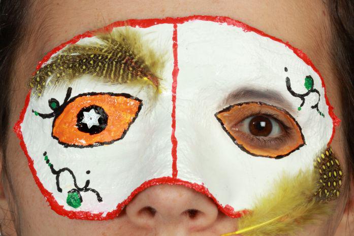 Das Gesicht eines Mädchens mit einer bunten Papiermaske und zwei Federn